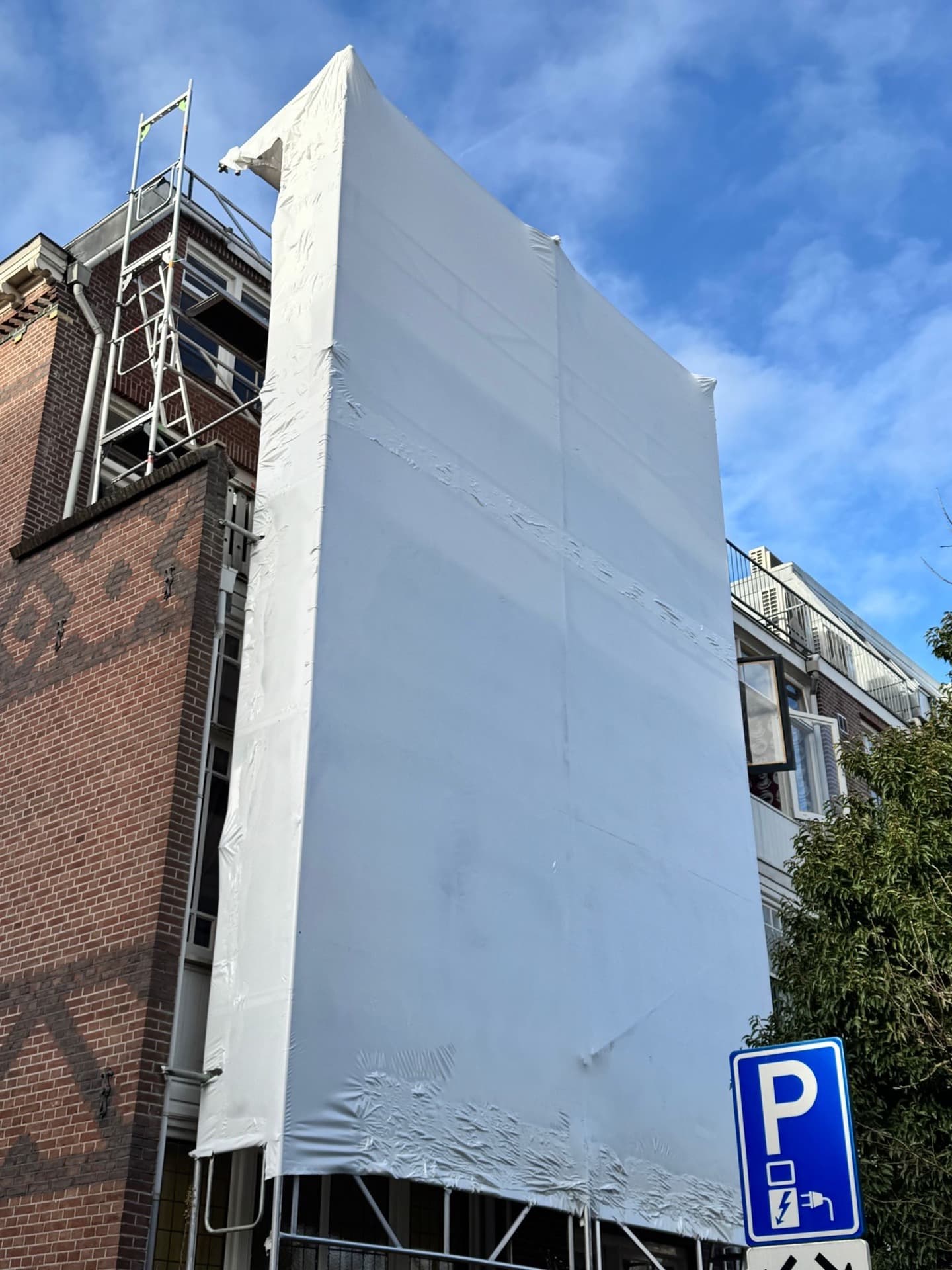 Hoge gevelsteiger bij bakstenen gebouw met veiligheidsfolie — professionele steigerbouw