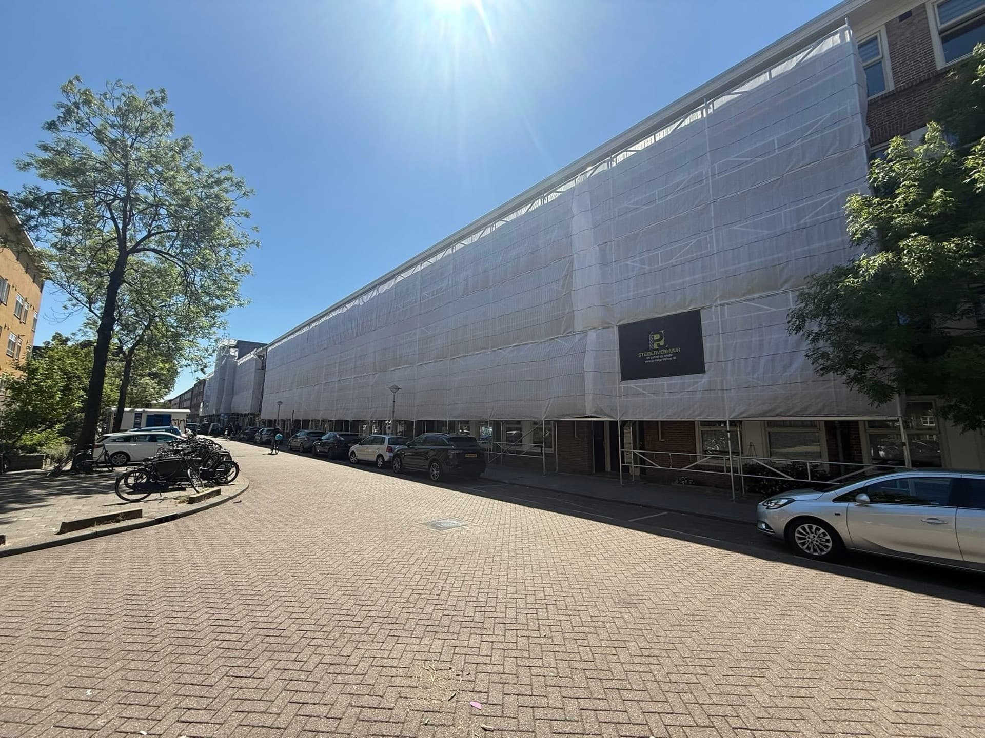 Langgerekte steigerconstructie langs woon- en winkelblok met PJ Steigerverhuur branding