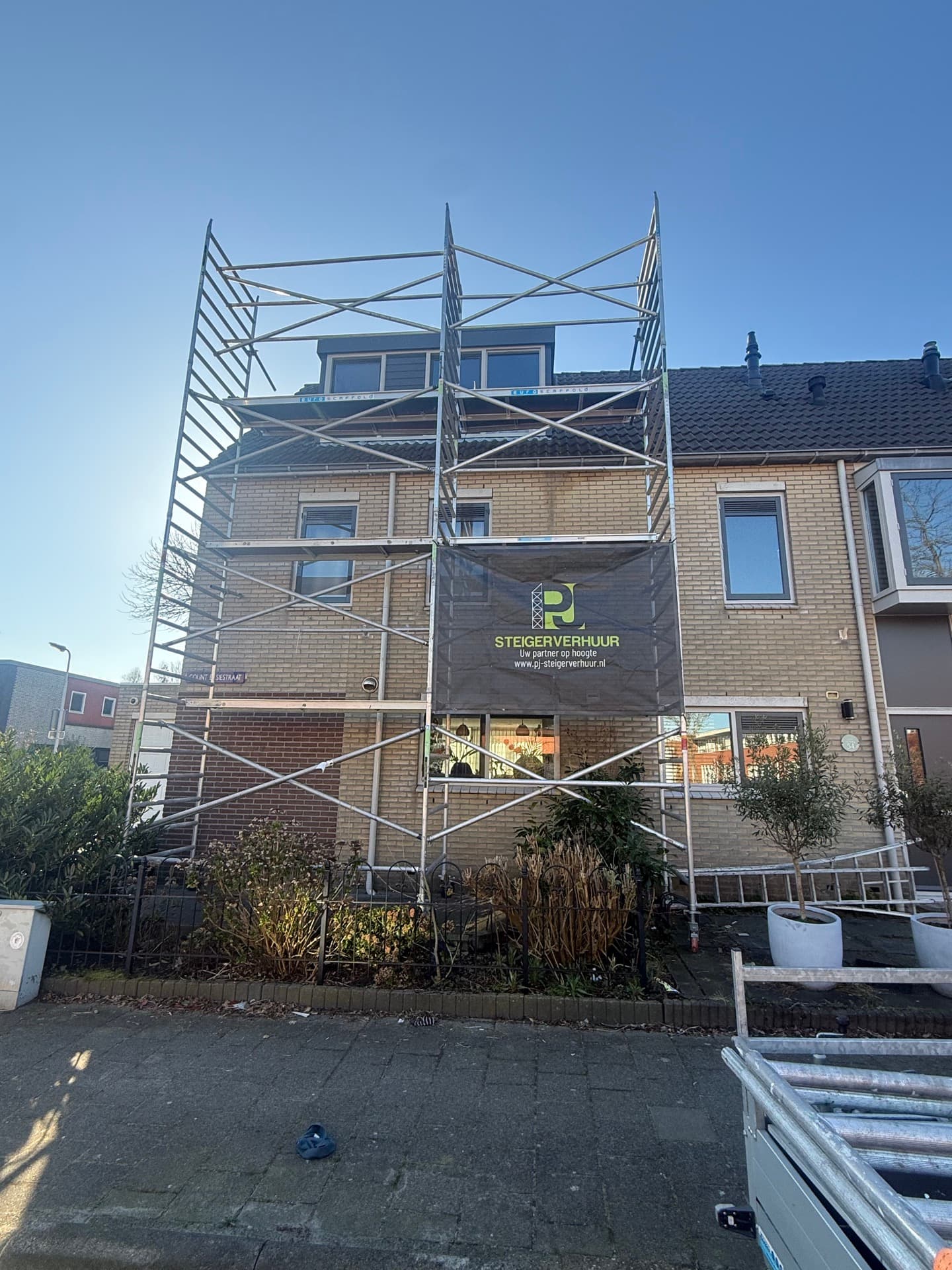 Rolsteiger huren — aluminium rolsteiger met PJ Steigerverhuur banner bij woonhuis